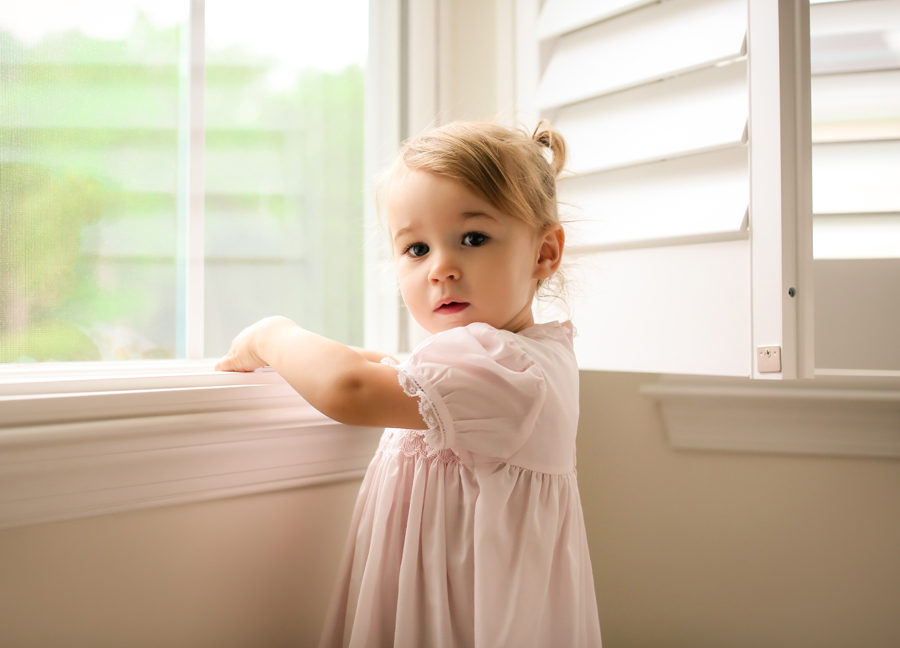 Image of a curious girl by the window at an in-home newborn session in Chandler, Arizona