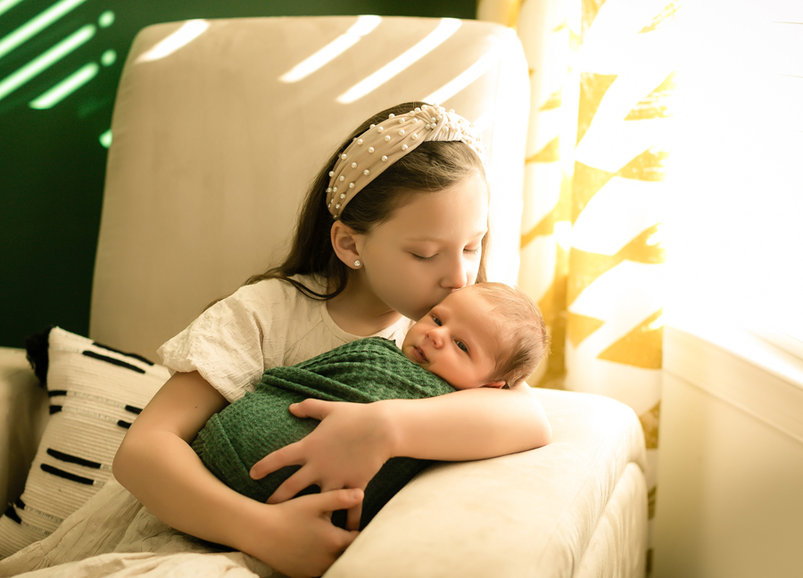 Image of a big sister kissing her baby brother at a newborn session in Scottsdale, Arizona