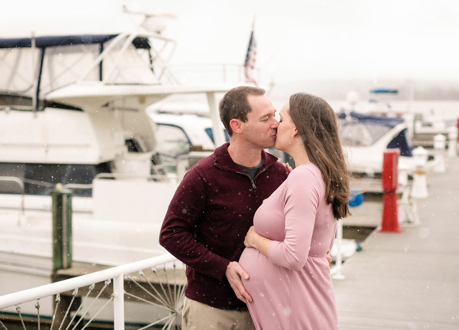 Old Town Alexandria Maternity Photoshoot with a couple kissing in front of boats.