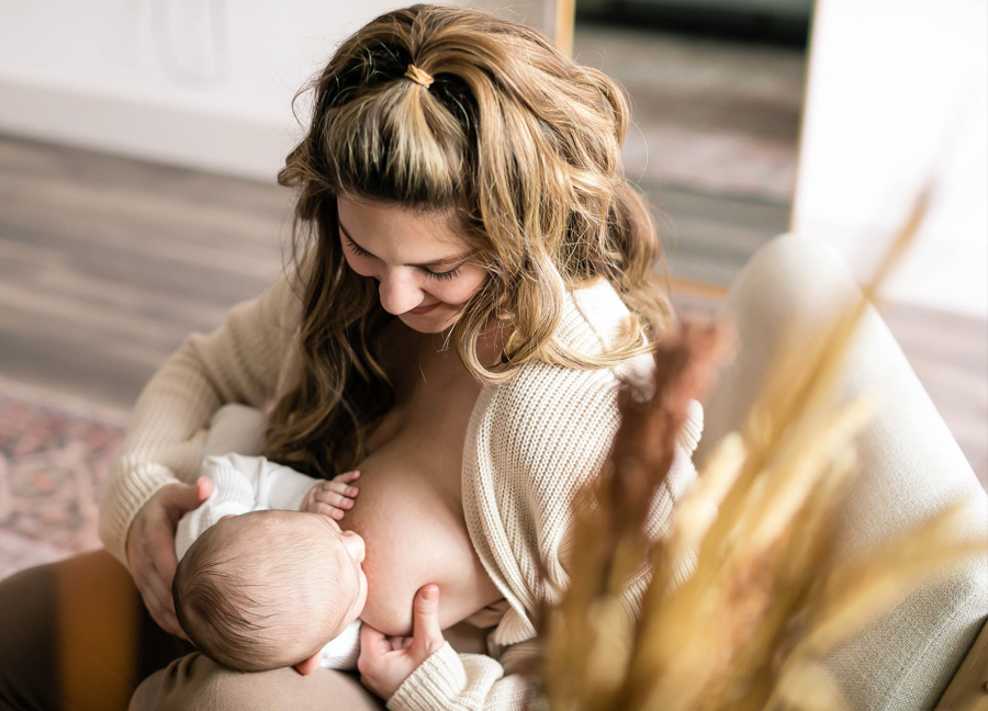 A mom breastfeeding her baby in a chair at a Northern Virginia newborn photography session with Stephanie Honikel Photography.