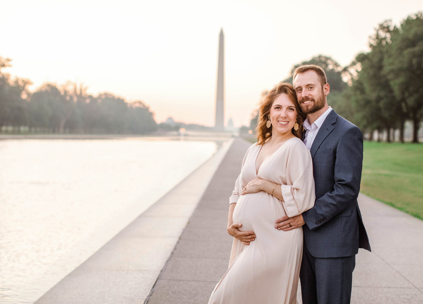 best prenatal massage in Northern Virginia series featuring A husband and wife smiling while posing for their maternity images with the National Monument in the background