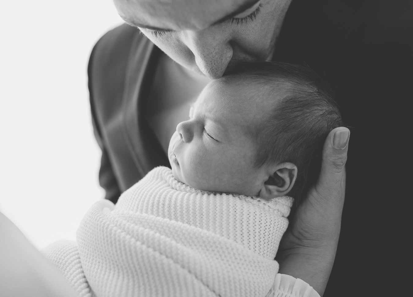 A black and white image of a dad kissing his newborn son on the head during a newborn session with Stephanie Honikel Photography 