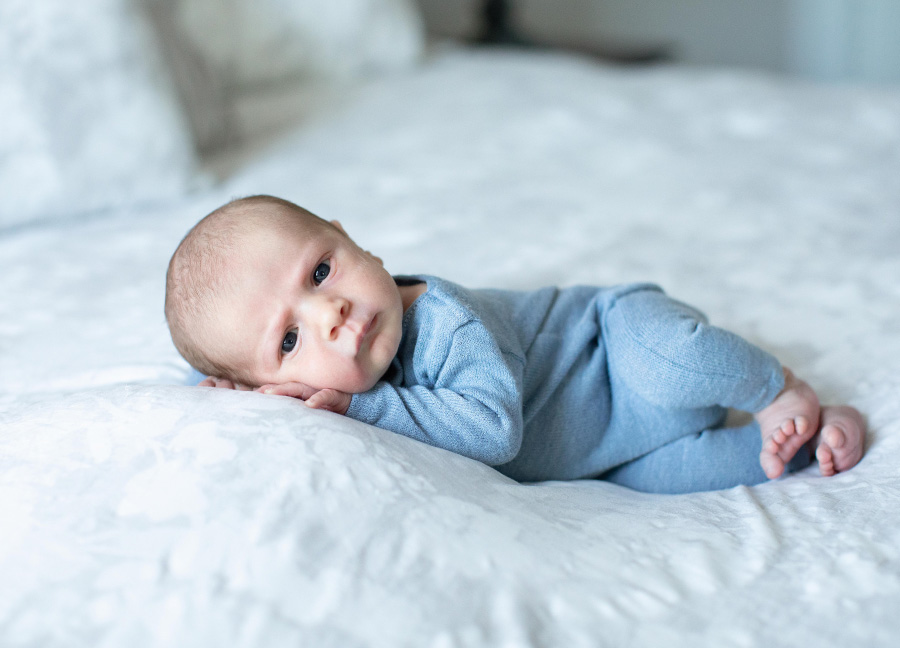 A wide awake baby boy in the side pose on a master bed - Lifestyle versus posed newborn photography