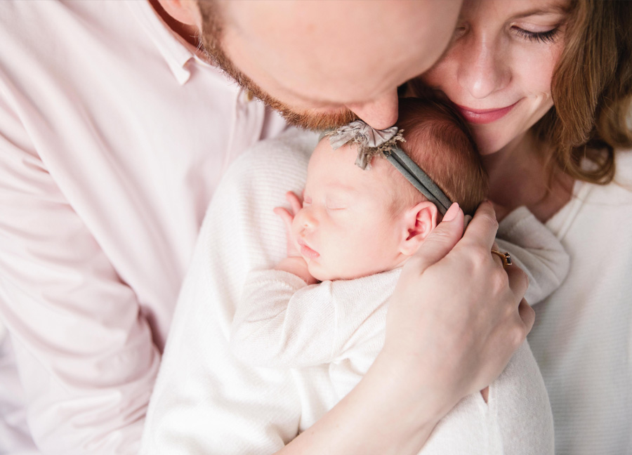 newborn photo session blog featuring a mom, baby, and dad kissing the forehead of their baby.