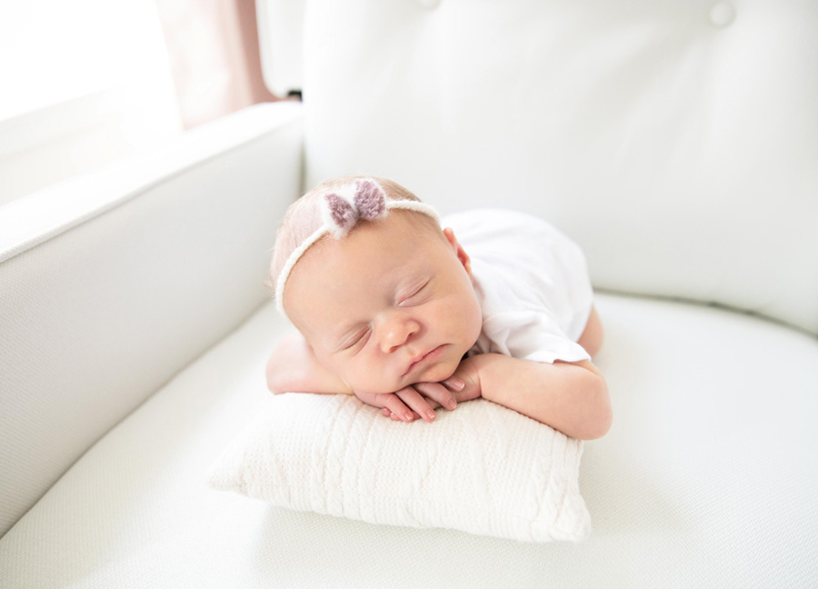 What props should I bring for a newborn photography session?featuring a baby girl posing on her hands on a pillow