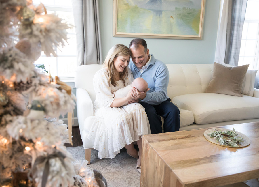 cozy D.C. Christmas newborn session at home featuring a mom, dad, and baby sitting next to a christmas tree