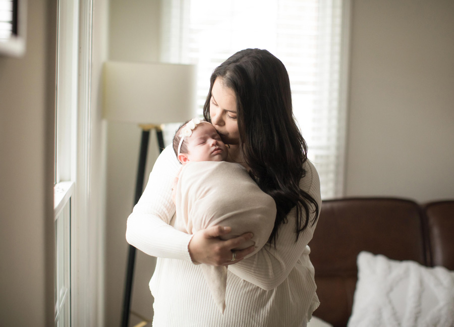 A mother kissing her newborn baby by the window during a Washington D.C. newborn photo shoot.