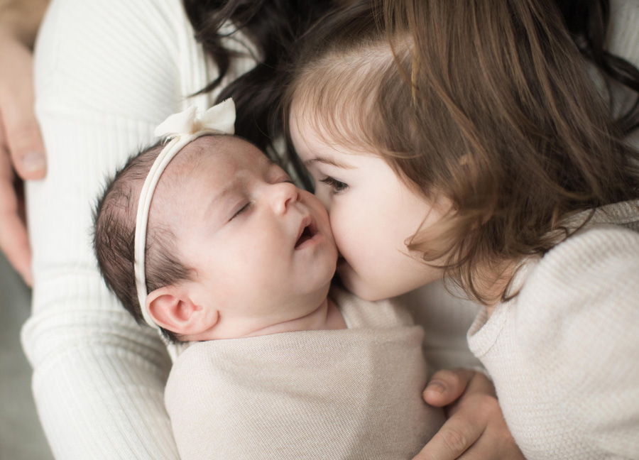 A toddler kissing her baby sister on the cheeks captured by Washington D.C. newborn photographer, Stephanie Honikel.