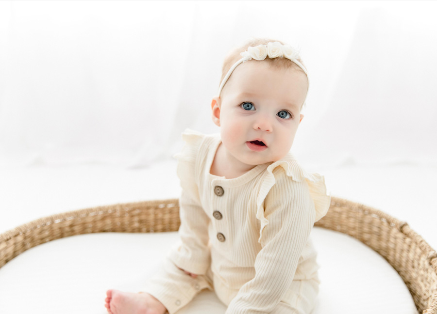 Baby girl in a white romper sitting in a basket during her baby milestone session in Washington, D.C.