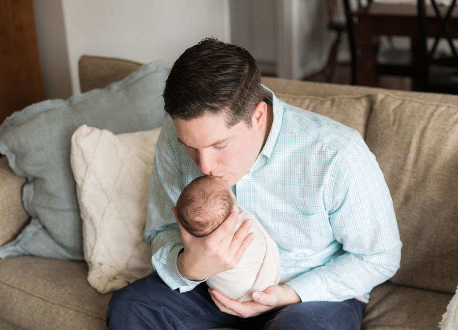 newborn photography with siblings featuring a dad kissing his newborn baby