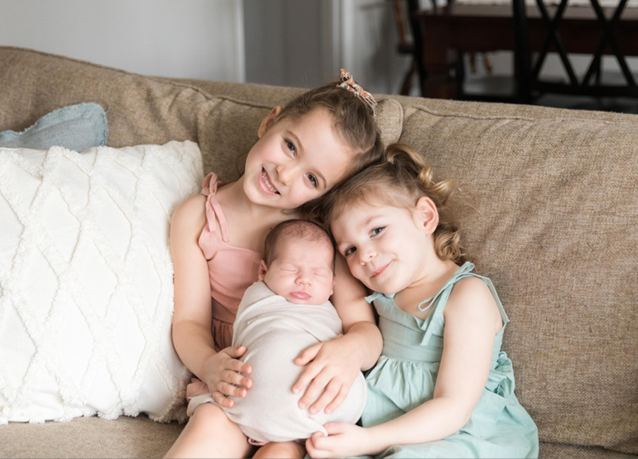 Two young girls cuddling with their baby sister during a newborn session with Stephanie Honikel Photography. 