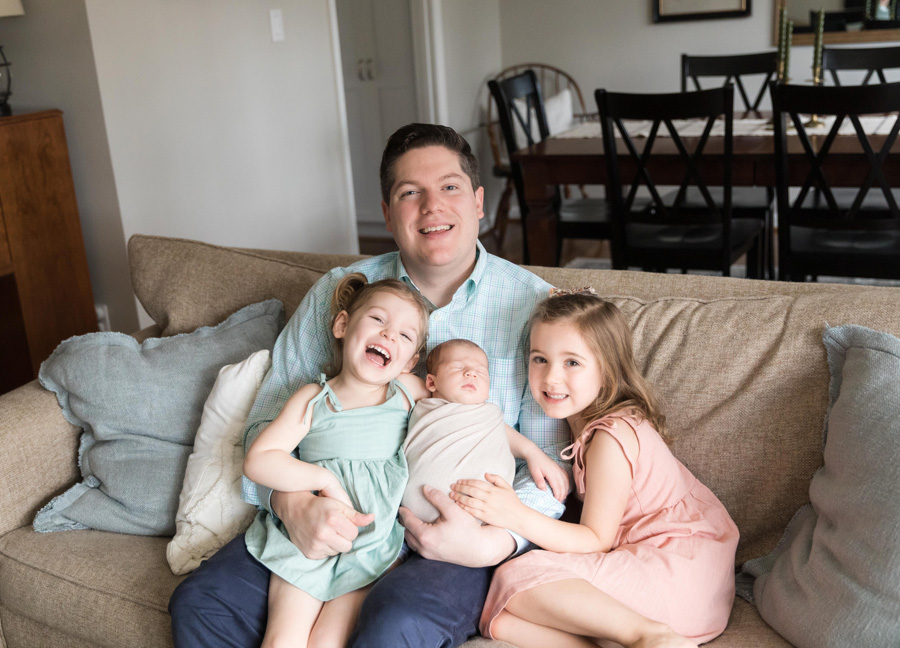 A father with his three young children sitting on a sofa during their newborn photography session in Northern Virginia. 