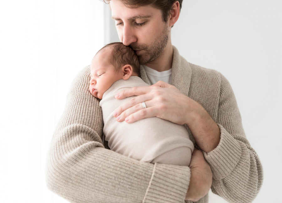 A swaddled baby boy in the arms of his father during a studio newborn photography session in Northern Virginia.