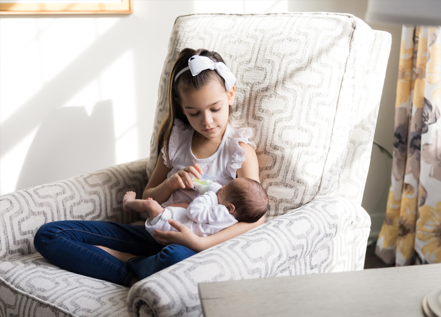 A girl bottle feeding her baby brother during an at home newborn photography session in Northern Virginia. 