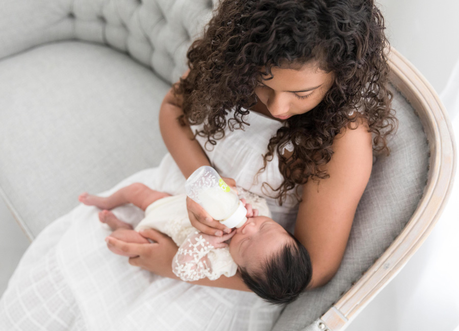 A girl bottle feeding her newborn baby sister at a newborn session with Stephanie Honikel Photography.