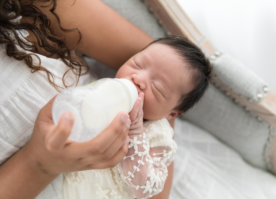 A close-up image of a girl bottle feeding her baby sister during her newborn studio session in Northern Virginia. 