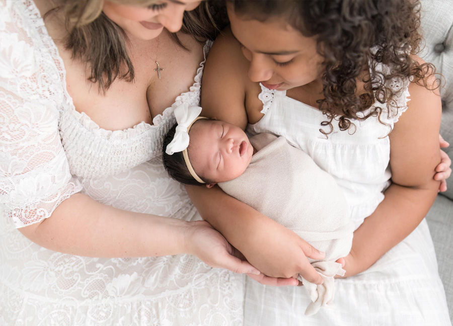 Image of a mother and girl holding a swaddled newborn baby during a studio newborn photo shoot.