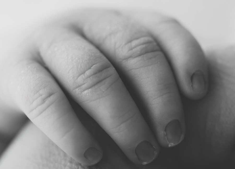 Black and white image of a baby's hands wrapped around her dad's finger.