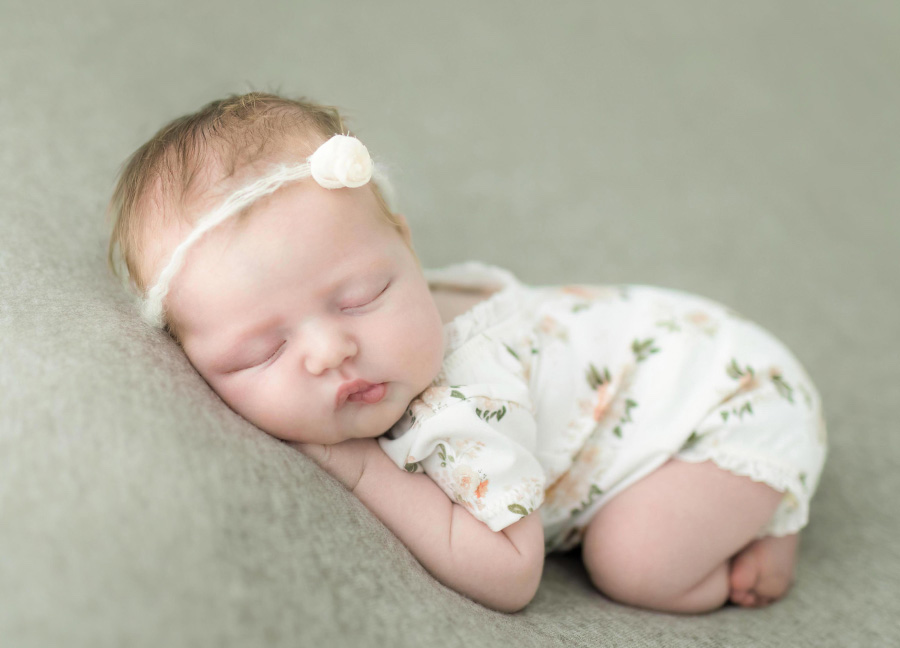 A newborn baby girl in a floral onesie sleeping on her side during her studio newborn session in Northern Virginia.