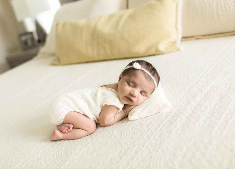 A baby in the tushy up newborn pose on the bed in her parent's master bedroom. 