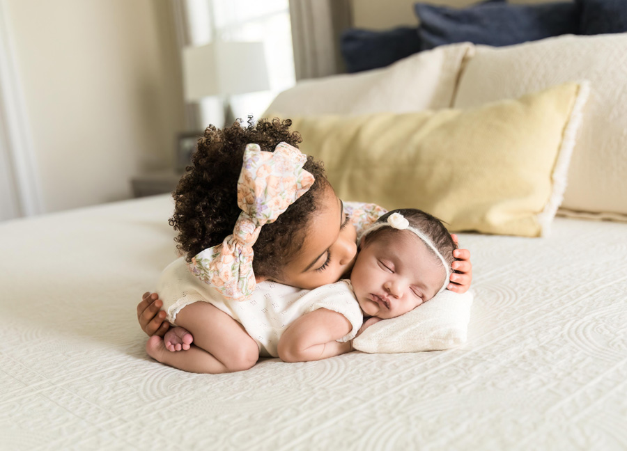 A toddler on her tummy kissing her baby sister who is posed in the tushy up newborn pose during their DC newborn photography session with Stephanie Honikel Photography.