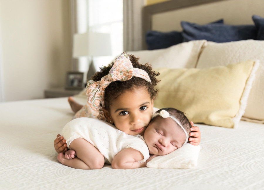 A toddler on her tummy cuddling with her baby sister who is posed in the tushy up newborn pose during their DC newborn photography session with Stephanie Honikel Photography.