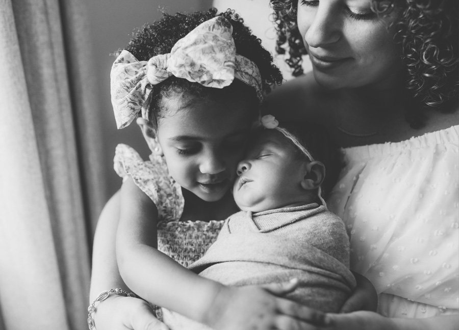 A black and white photography of a mother holding her toddler and newborn baby girl during their DC newborn photography session.