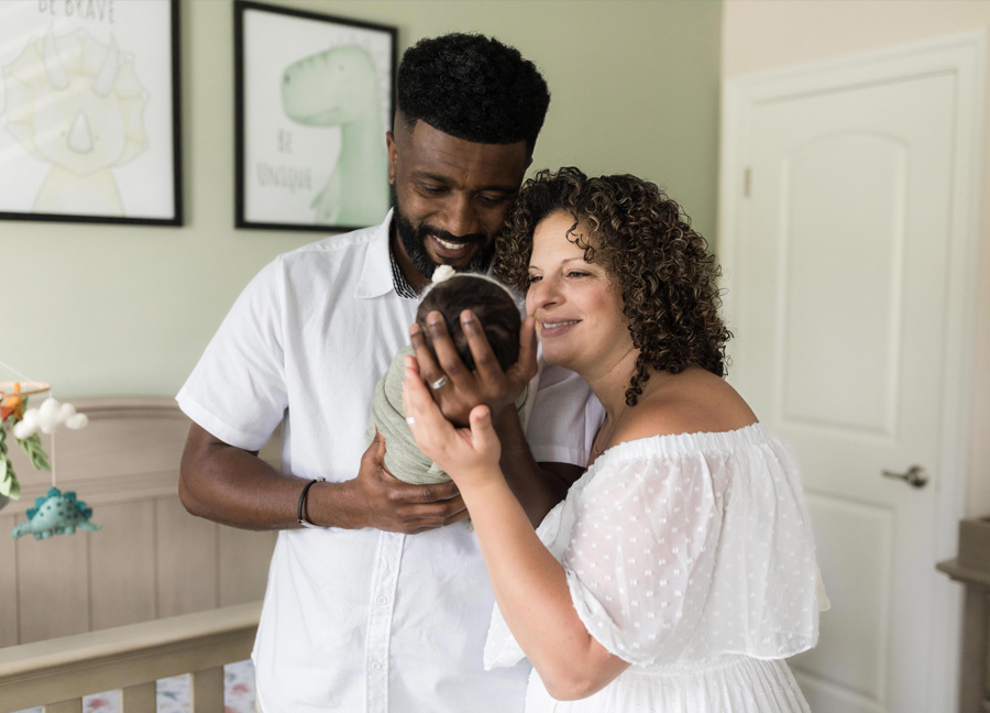 A mother and father looking at their baby girl while standing in front of the crib during their DC newborn photography session at home.
