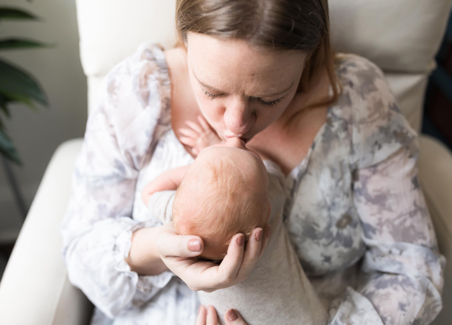 A mother kissing her newborn baby while sitting in the rocking char during their newborn session with Northern VA baby photographer, Stephanie Honikel. 
