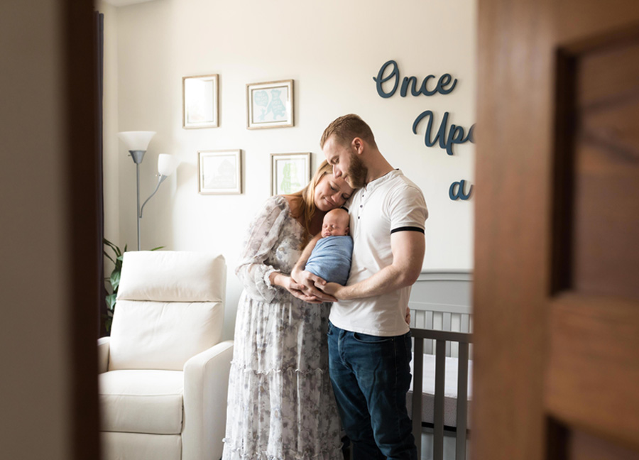 A mother and father holding their swaddled baby boy while standing in front of a crib during their in-home newborn session in Washington, D.C.