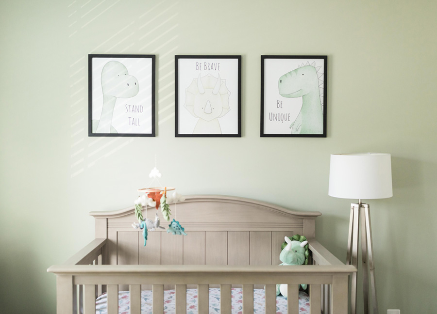 gender neutral nursery with a crib, dinosaur mobile, three dinosaur pictures that are framed with a light green painted wall.