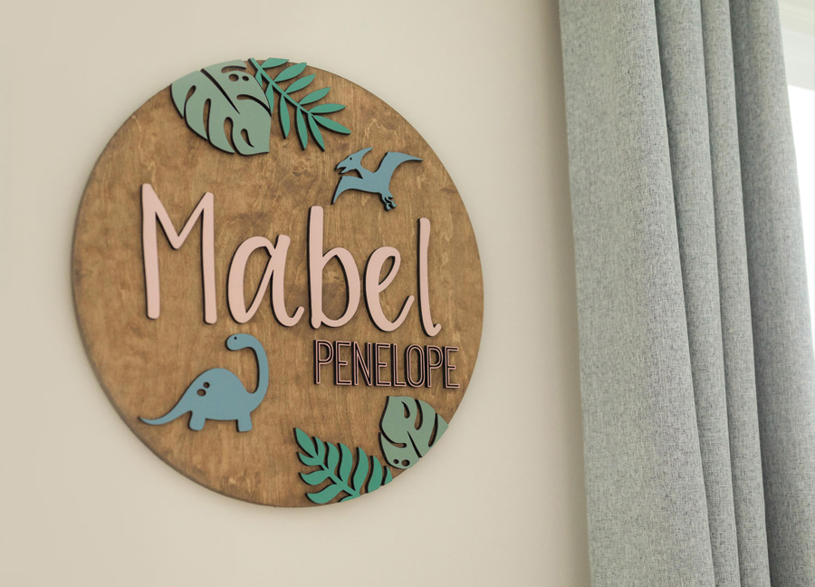 the name Mabel Penelope on a circle dinosaur-themed plaque for the gender neutral nursery