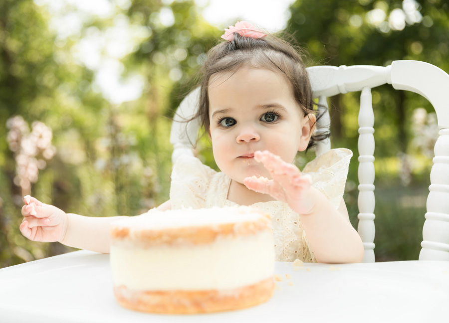 first birthday milestone photograph shows a little girl reaching for her cake