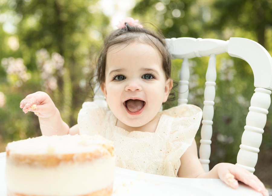Baby laughing in front of her cake during her first birthday milestone portraits