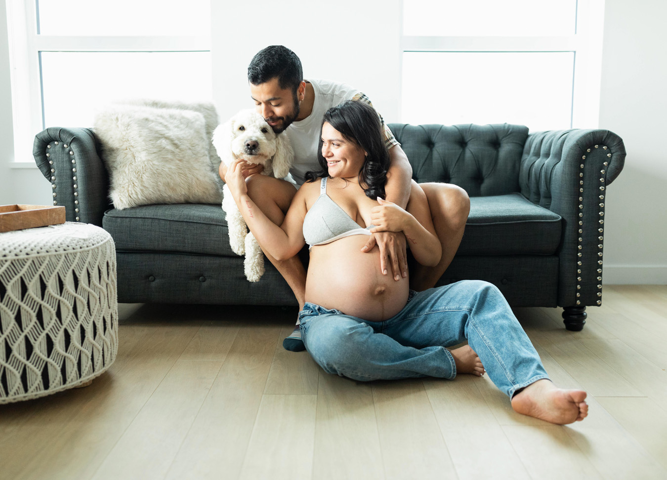 Pregnant woman sitting on the floor with a man and a dog sitting on the couch above her