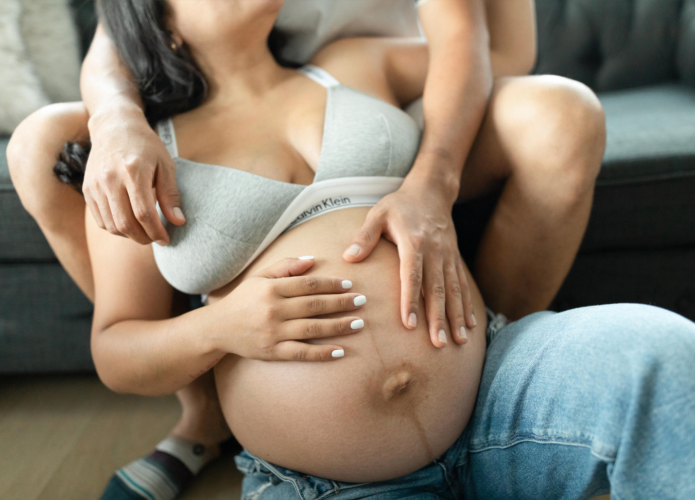 Pregnant woman's belly with her hand on it, embracing her partner sitting above her.