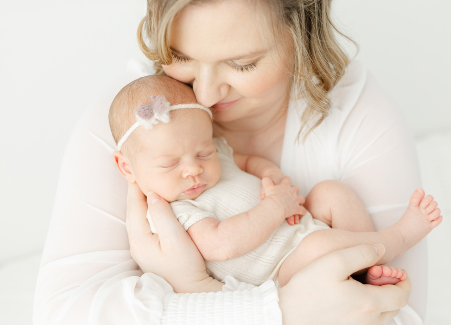 Mother gently holding her sleeping newborn baby in a soft, light-filled studio, capturing a tender and timeless newborn photography moment