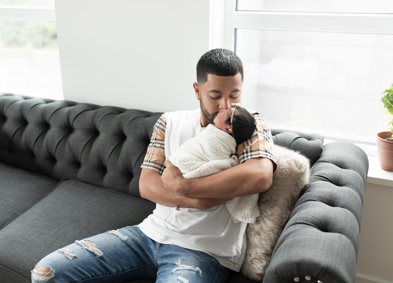 DC Birth Centers, dad holding newborn baby, sitting on a couch and giving her a kiss. Photographed by a newborn photographer in D.C.