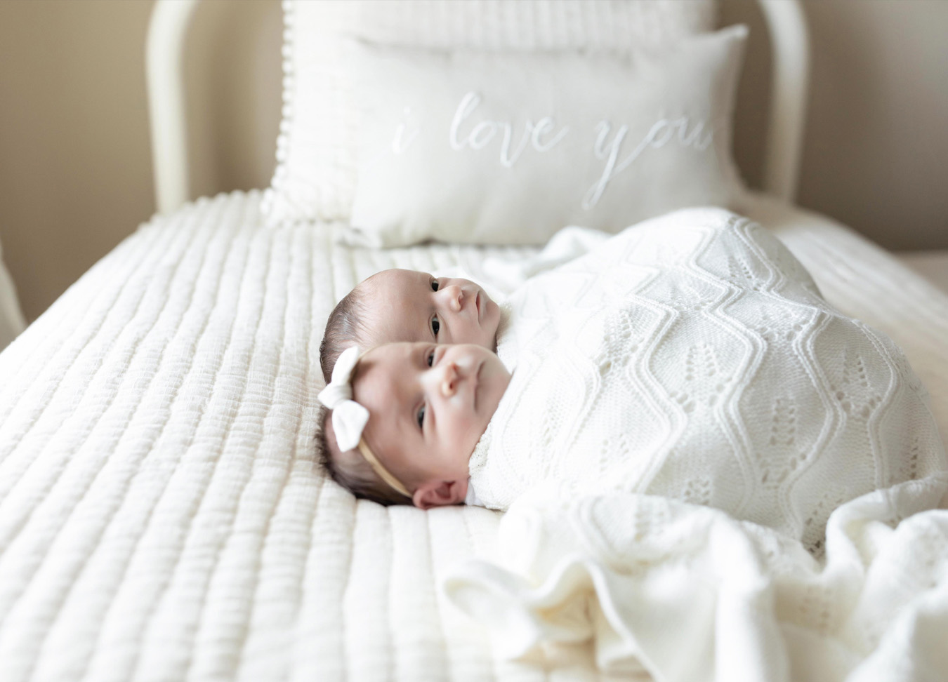 twin newborn session with both babies laying on a bed bundled up.