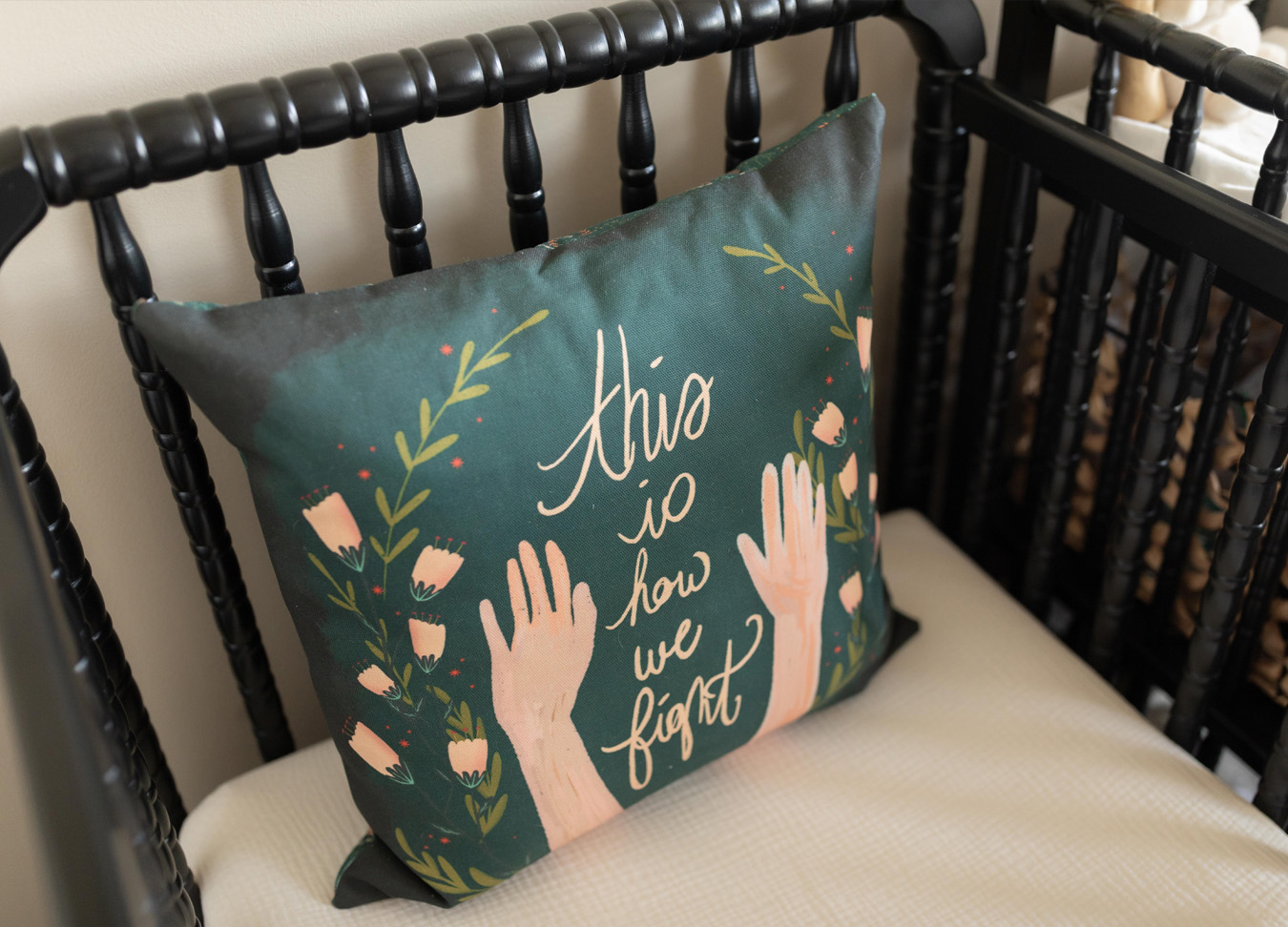 green pillow with the phrase "this is how we fight" is sitting in a black crib.