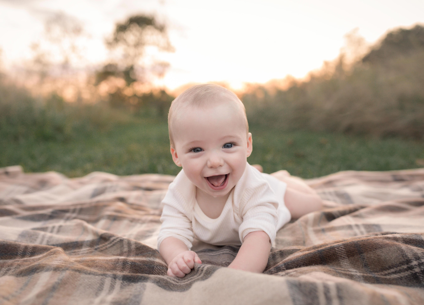 A smiling baby boy on his tummy at sunset during a family session at Rust Manor 