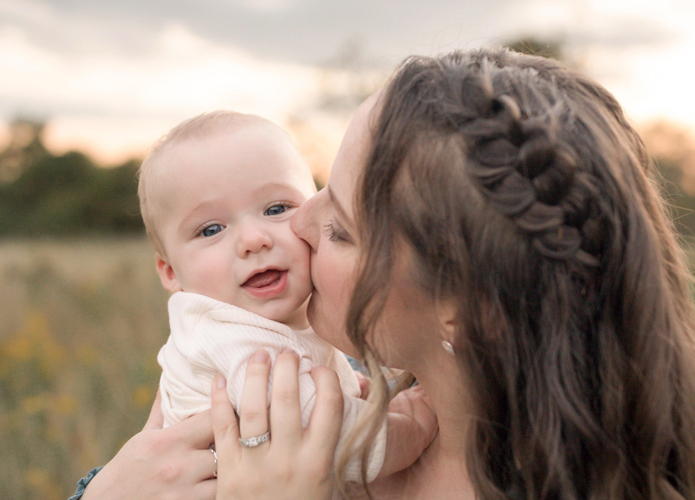 A mother kissing the cheeks of her baby boy during a sunset family session at Rust Manor 