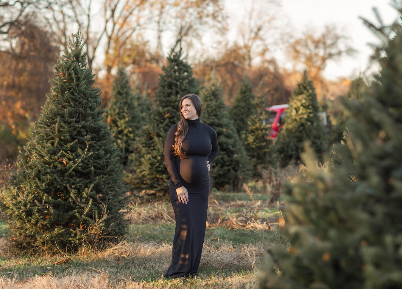 Christmas Maternity Photoshoot in Northern Virginia featuring a pregnant woman smiling at a tree farm.
