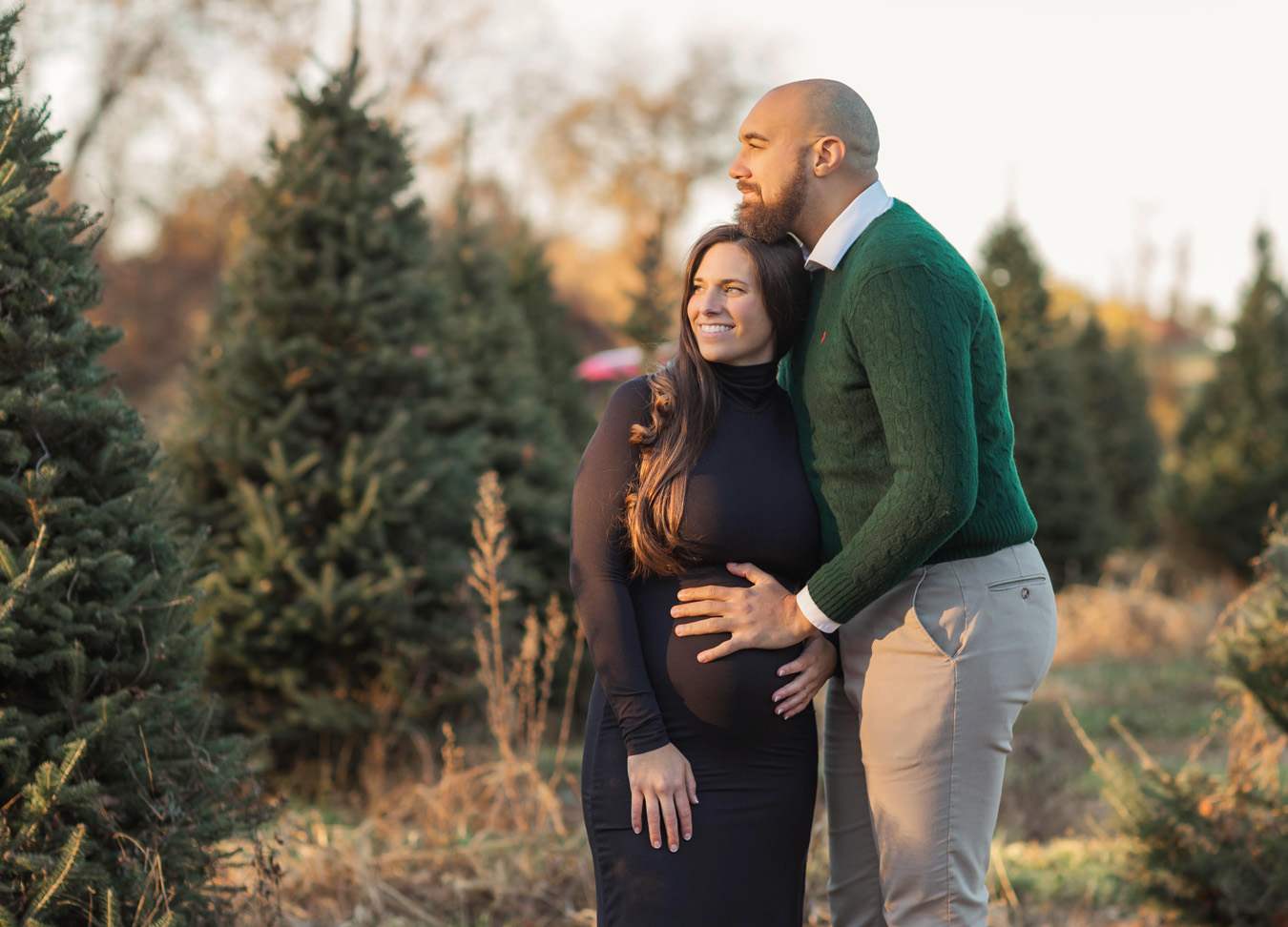 Pregnant woman and her husband standing in the middle of a tree farm