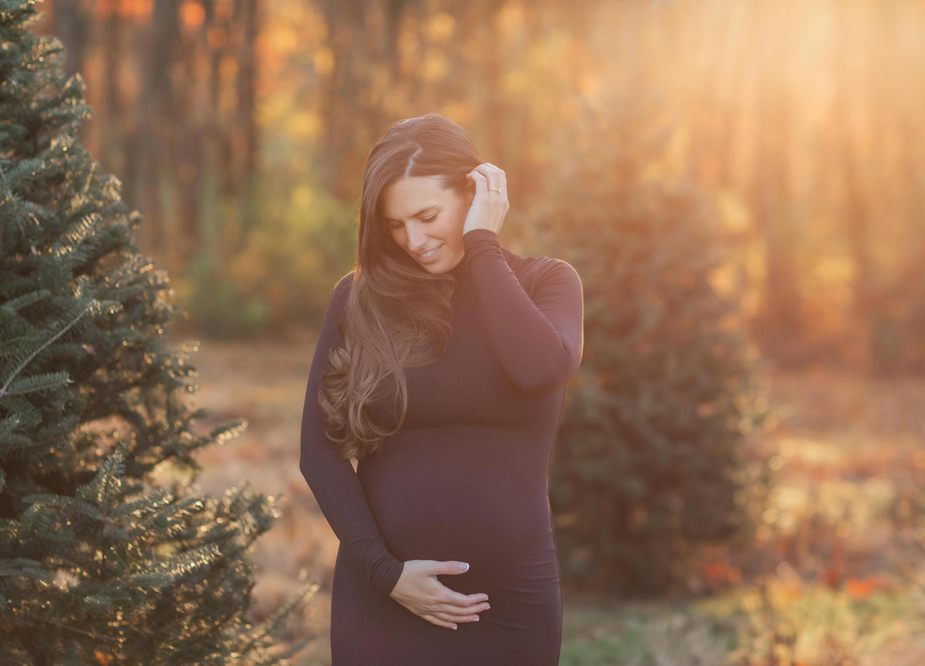 pregnant mom grabbing her stomach and smiling while the sun comes in between the leaves