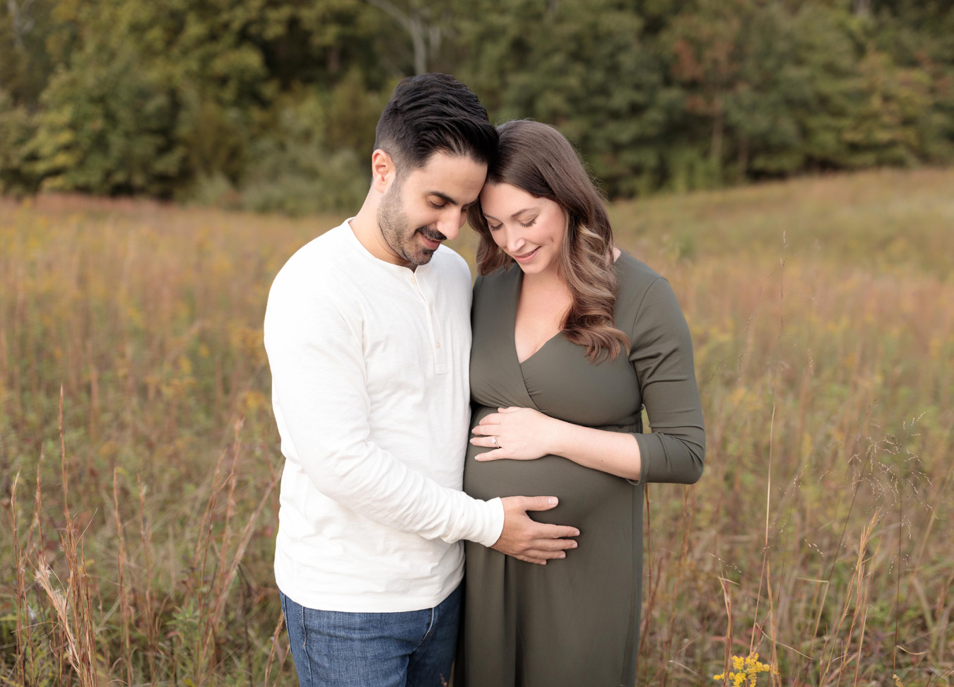 pregnant mother and her male partner standing in a field, holding her stomach shot by a northern virginia maternity photographer