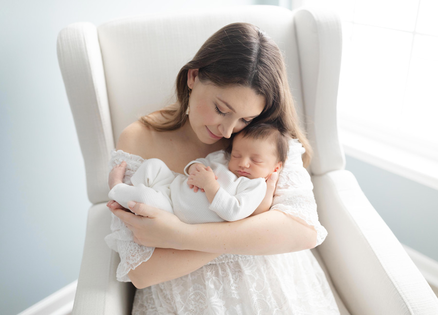Mom snuggling a baby in a white chair taken by a Washington D.C. newborn photographer