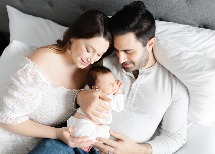 mom, dad, and baby snuggling on the bed captured by a newborn photographer in Washington D.C.