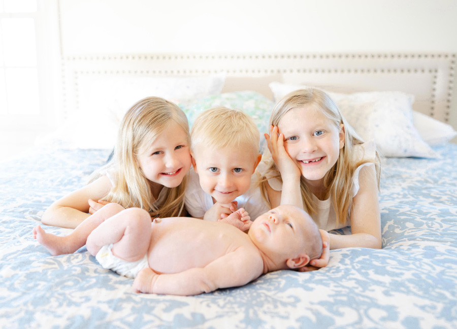 stress of motherhood  article featuring three kids smiling and cuddling their newborn baby sibling