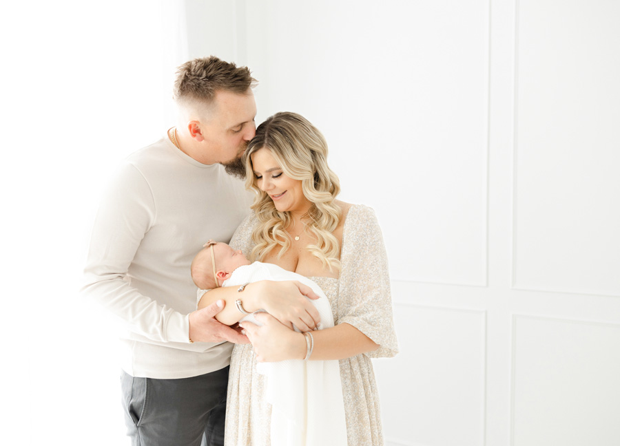 a man and woman holding a baby in a white swaddle blanket